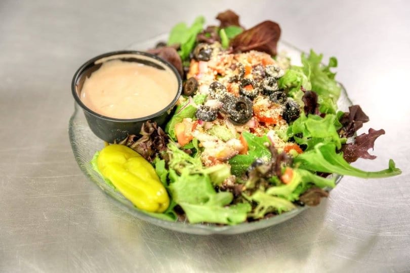 Fresh garden salad with mixed greens, tomatoes, olives, cheese, a pepperoncini, and dressing.