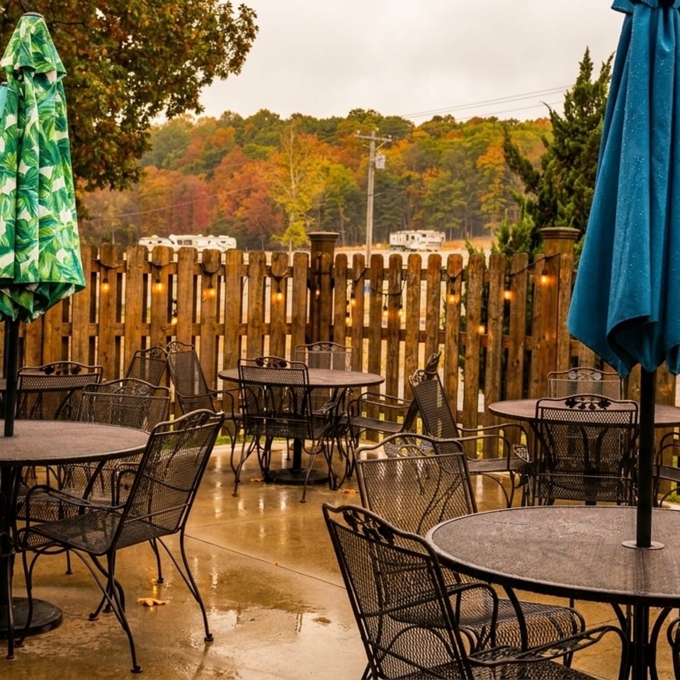 Outdoor patio with metal tables and chairs, umbrellas, and a wooden fence with string lights.