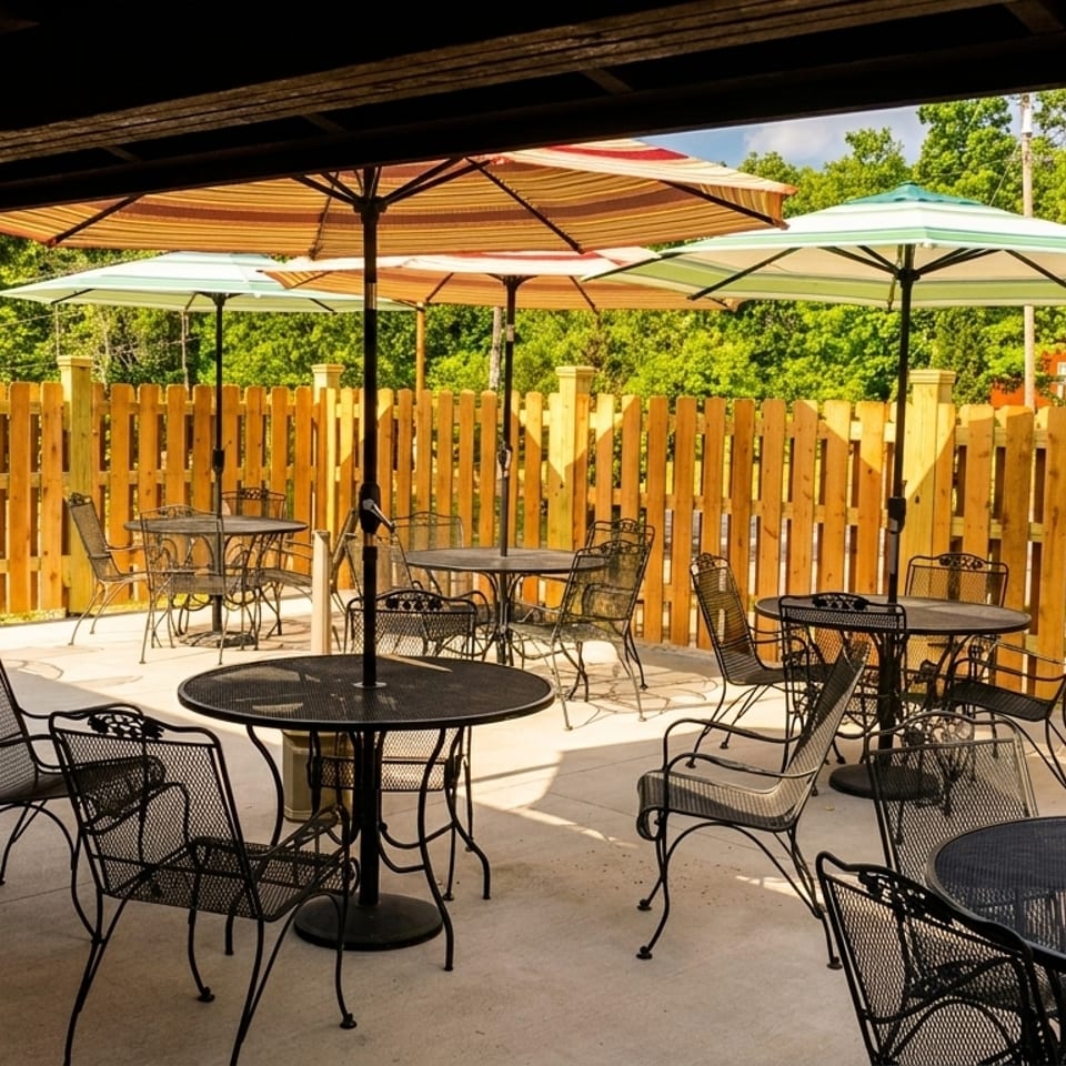 Outdoor patio with black metal tables and chairs, striped umbrellas, and a wooden fence.
