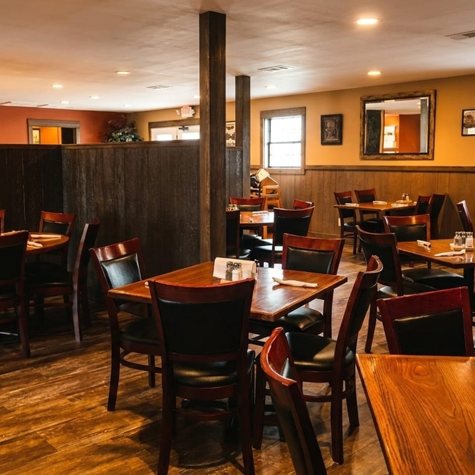 Warmly lit restaurant dining room with wooden tables, dark chairs, and wood-paneled walls.